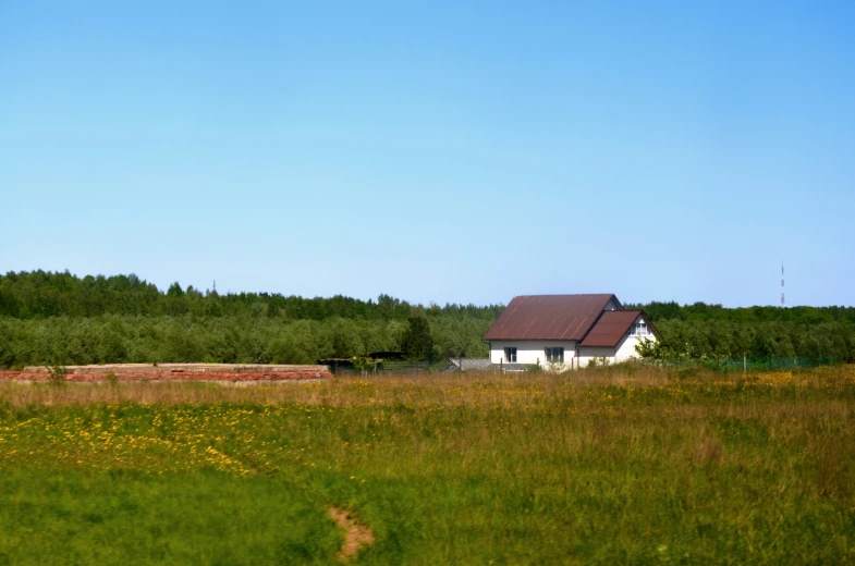 a house and field in the countryside under a blue sky