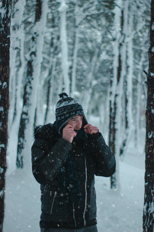 person in winter clothing looking through trees with snow falling