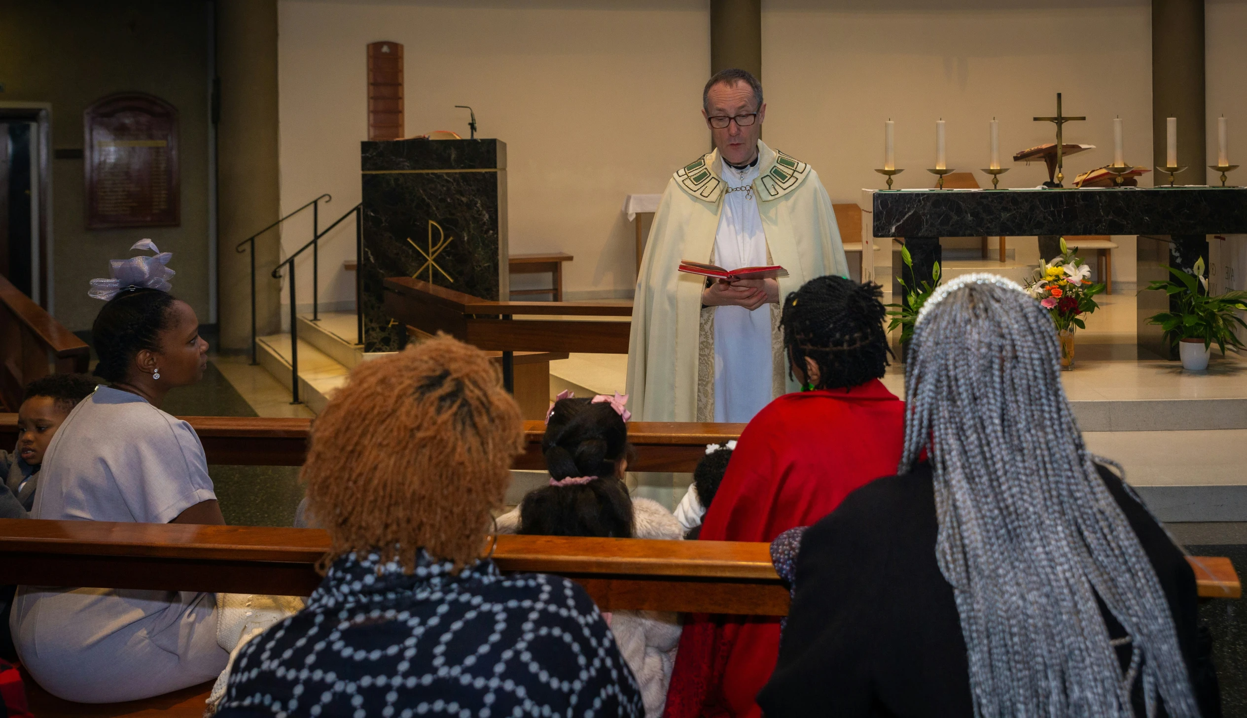 the man stands before people in red dresses in a church