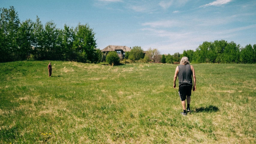 man walking in grassy field near house with trees