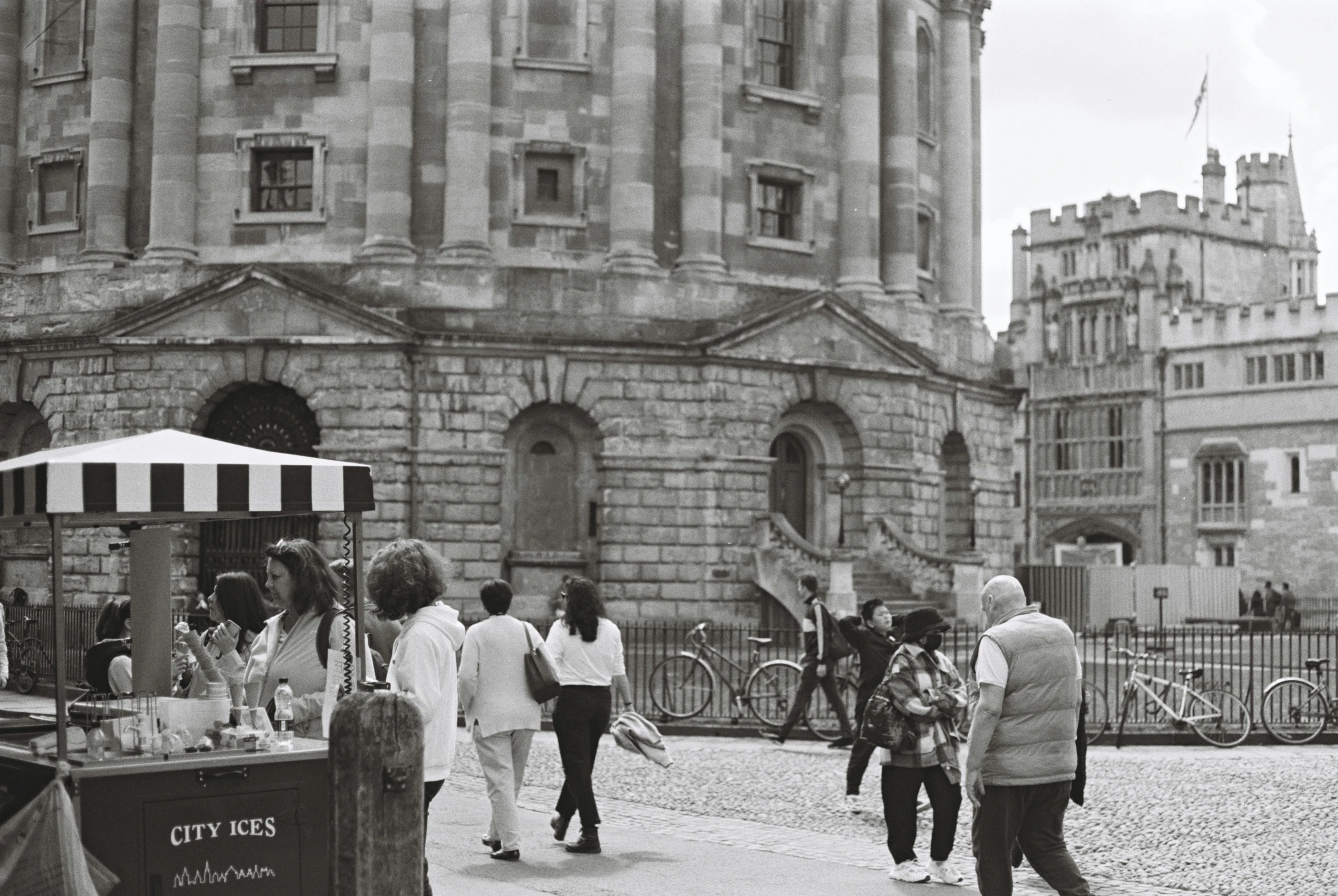 a black and white picture of people on the sidewalk in front of buildings