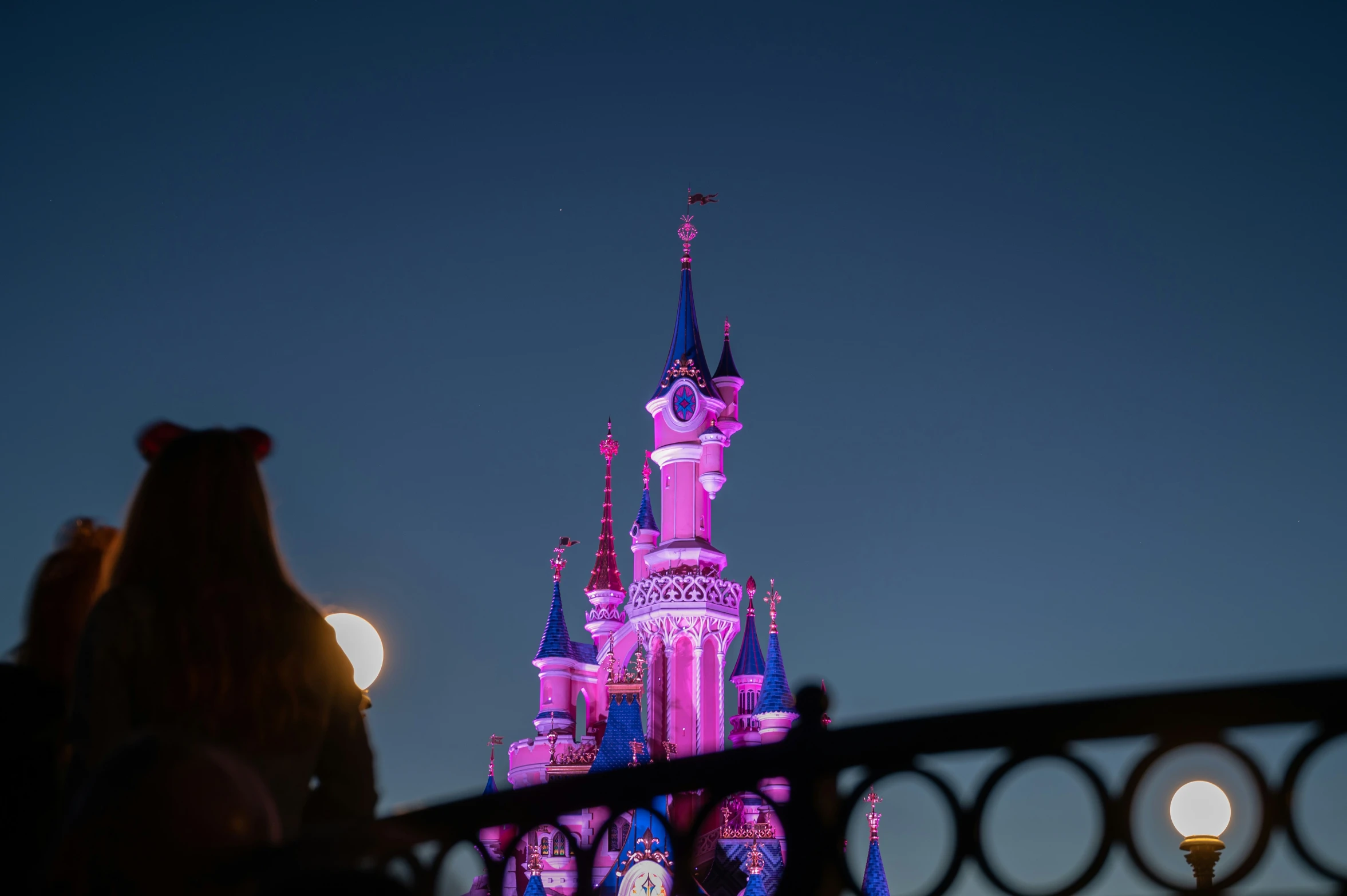 people walking by a large pink castle with lights