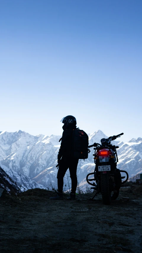 person with back pack standing by motorcycle at sunset