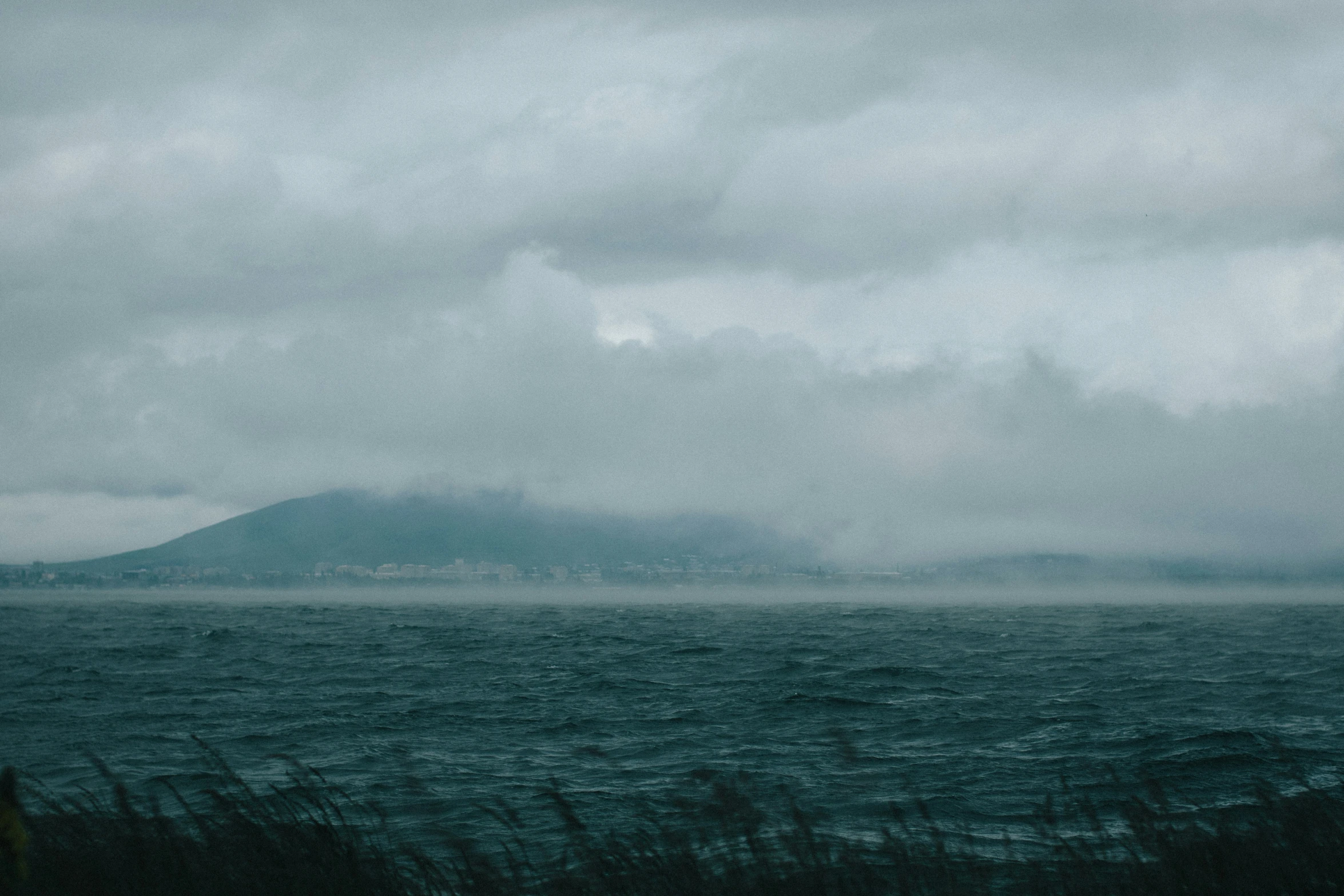 the ocean with some clouds and a big island in the distance