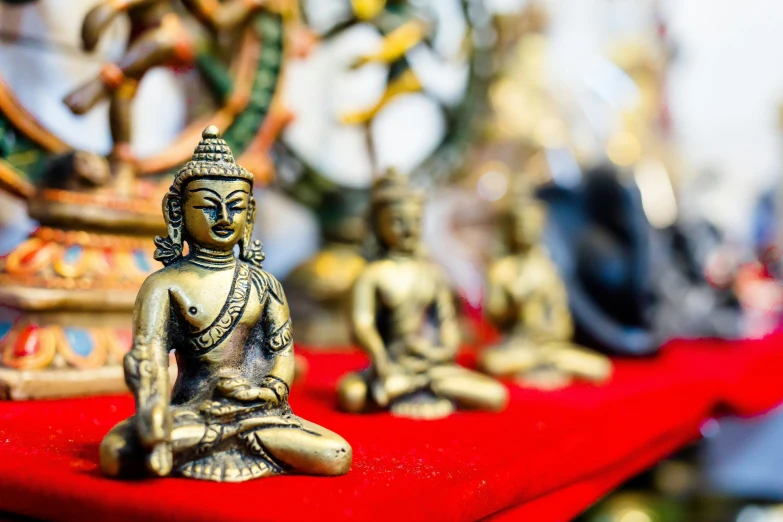 buddha figurines sit on a red mat in front of ornate artwork