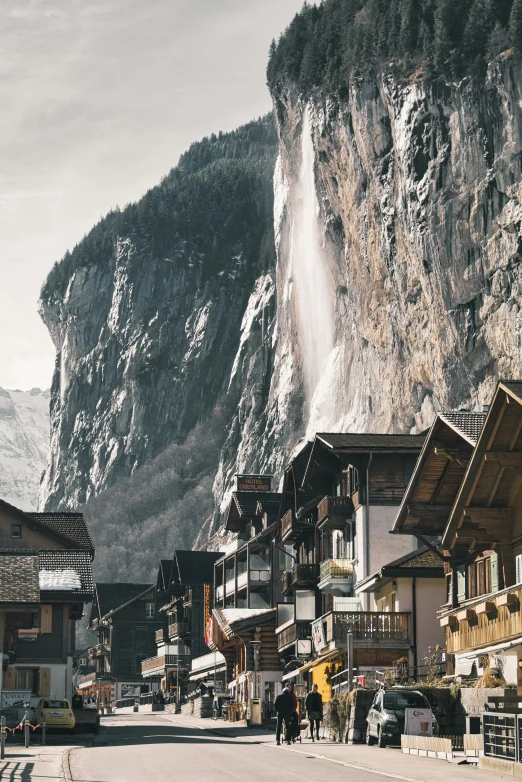 some buildings and people walk in a town in front of a mountain