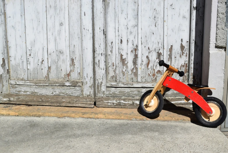 small wooden toy bike parked outside an old barn door