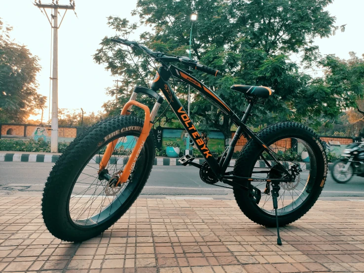 an orange and black mountain bike on brick road next to trees