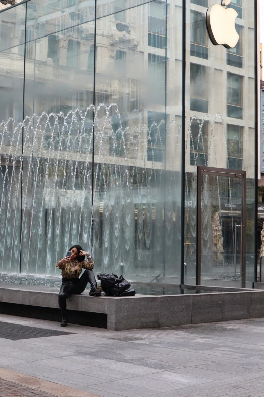 there is a person sitting on the ground using his phone near an apple store