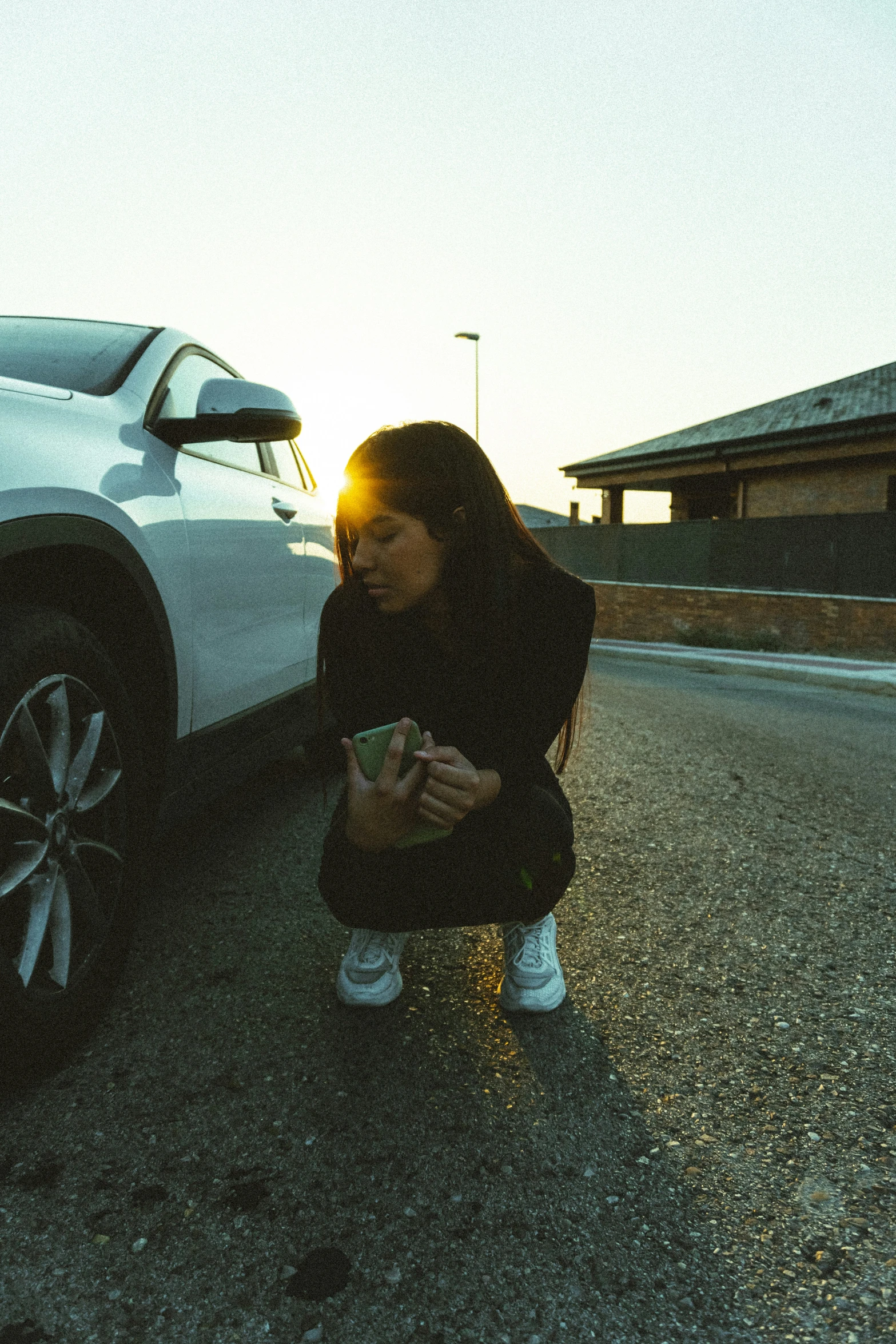 woman crouched down next to parked car with sun shining through the windshield