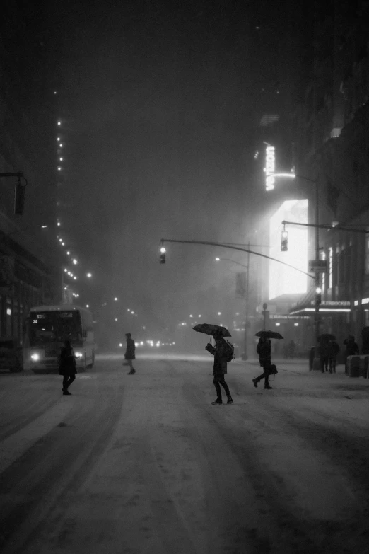 black and white pograph of people holding umbrellas in the snow at night