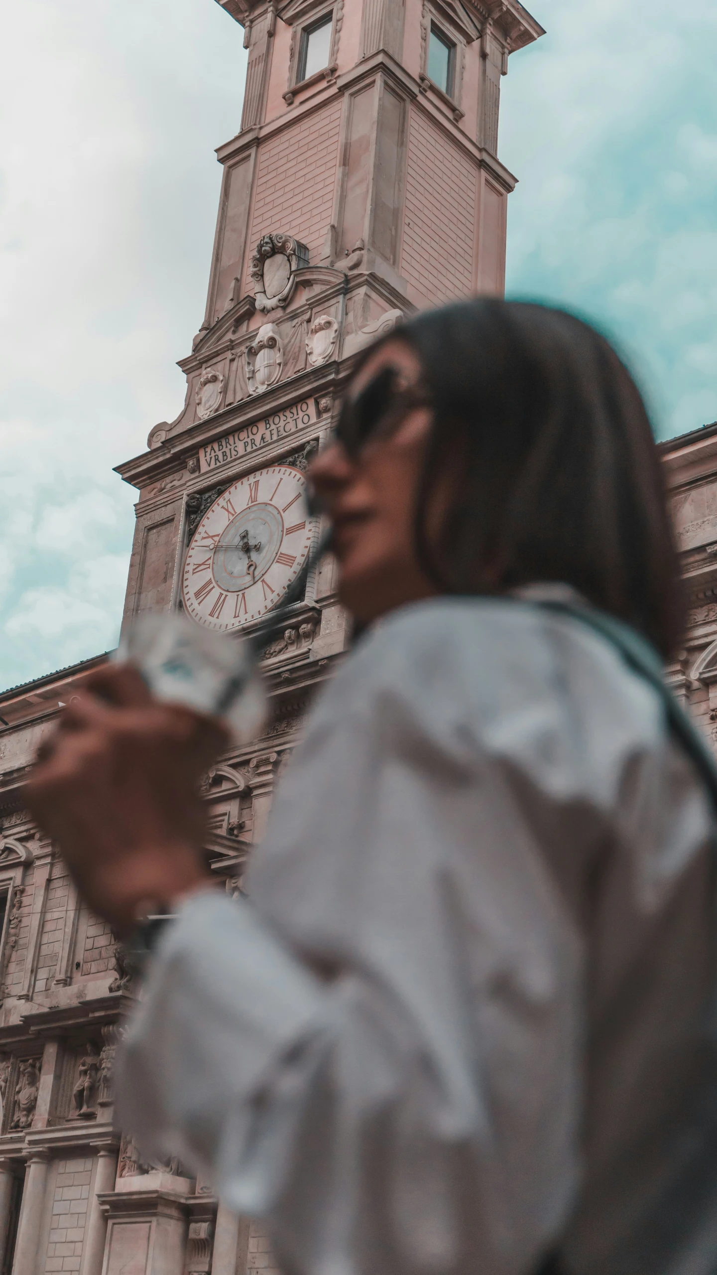 woman in sunglasses holding water in front of a large building