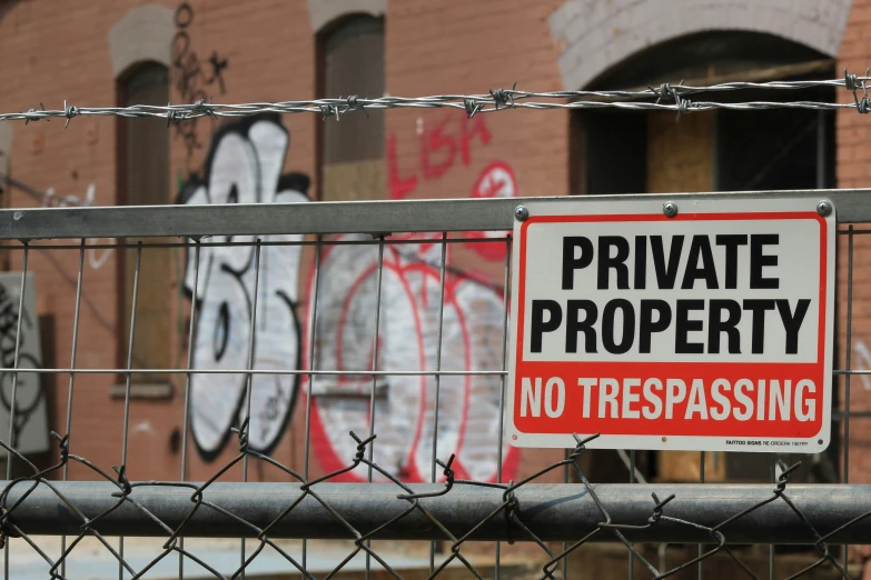 a private property sign on a metal fence with graffiti