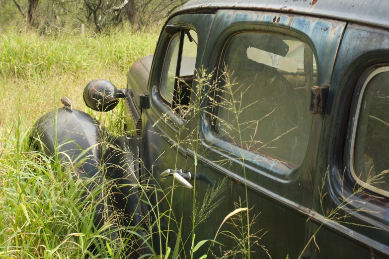 an old black car parked in a field with tall grass