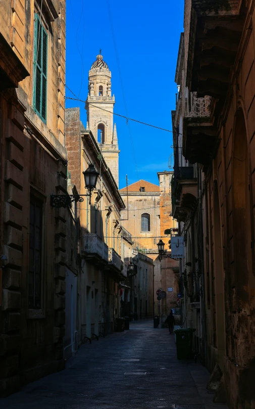 a narrow alleyway with stone buildings and a clock tower