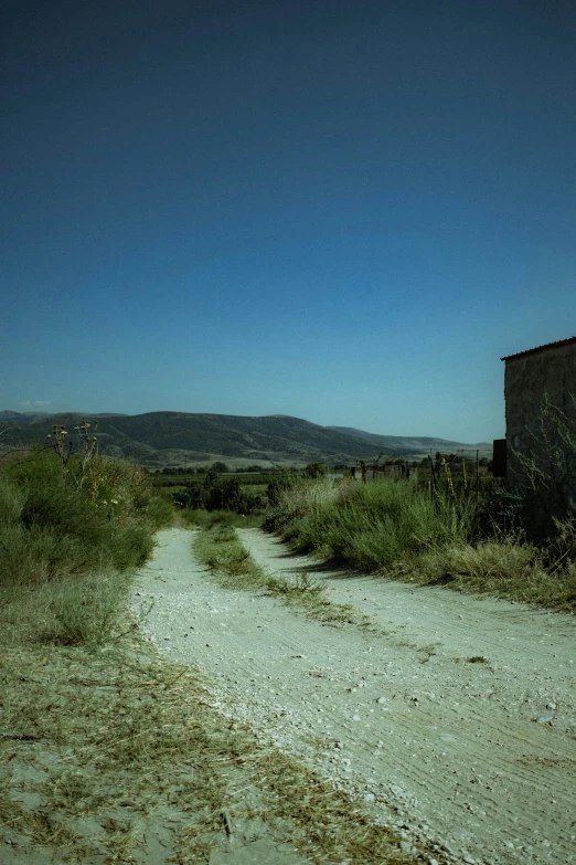 the dirt road is running parallel to the grassy hills