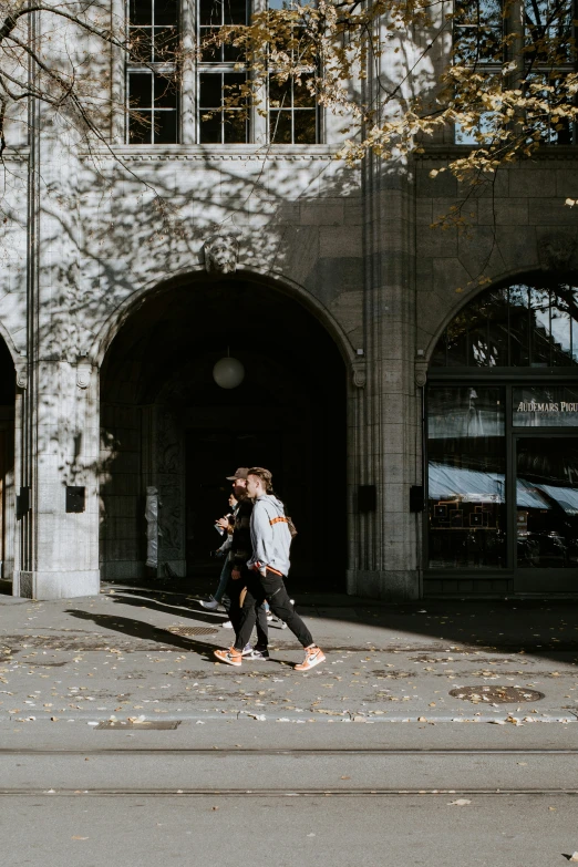 two men walking past a stone building with arched doors