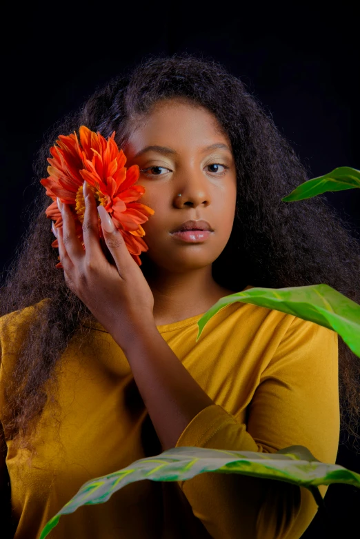 the girl in the yellow shirt is holding a orange flower