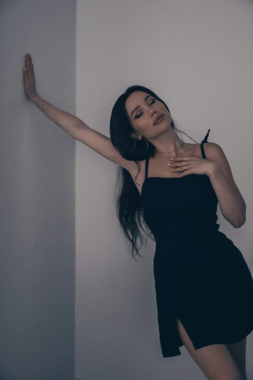 a woman is leaning against a wall wearing a black dress