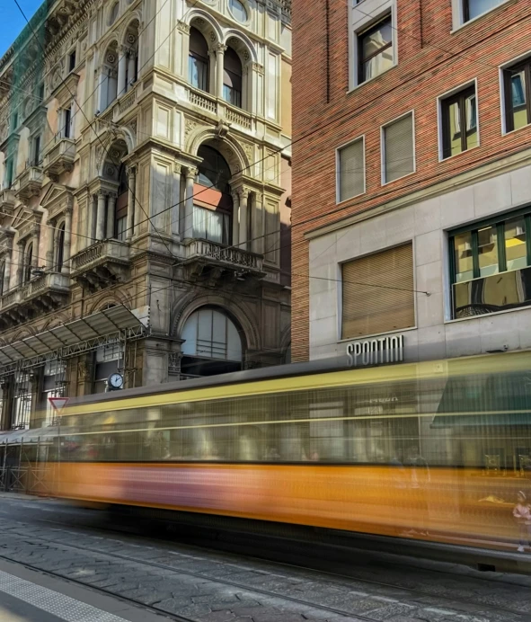 an orange and yellow tram speeding past tall buildings