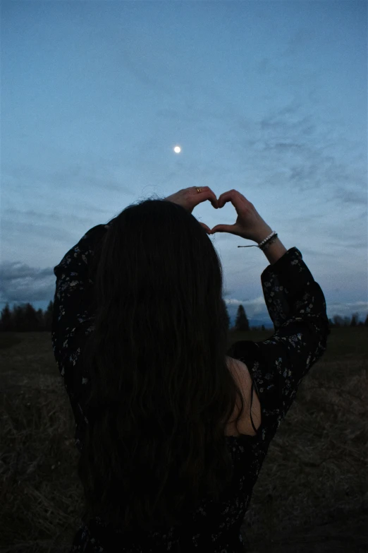 a woman making a heart shape in the middle of a night sky