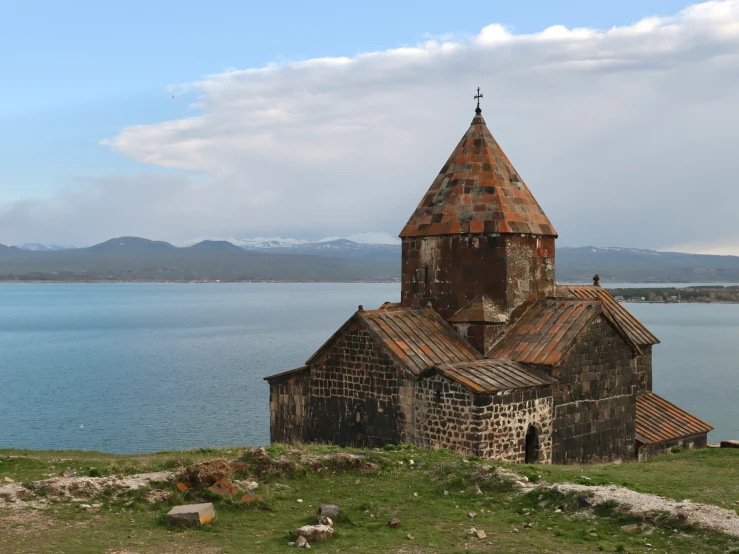 an old, rust - toned church is perched on a small hill overlooking the sea