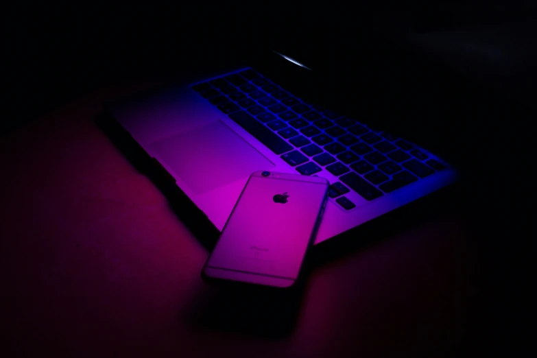 a pink iphone laying next to a purple laptop