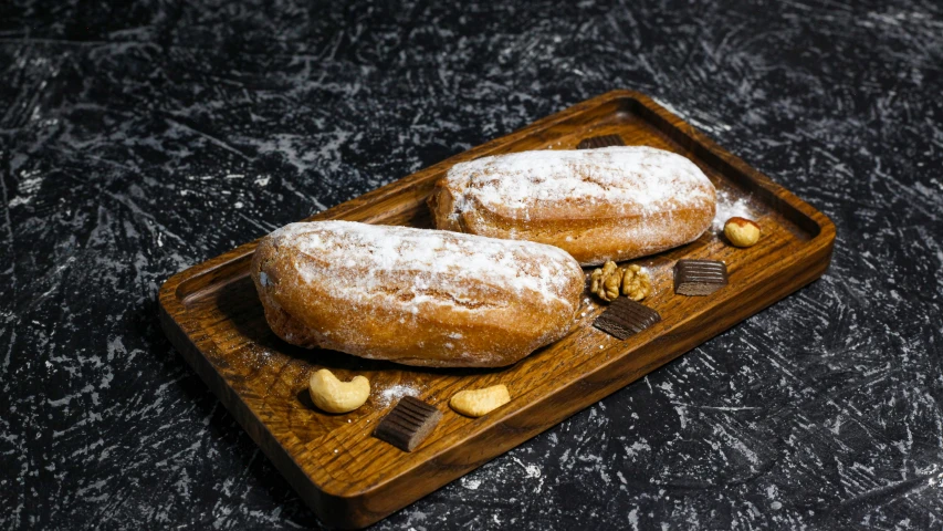 two chocolate covered pastries sitting on a wooden tray