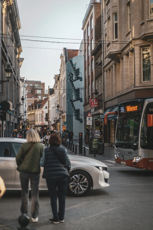 two people walk by the sidewalk as one crosses the street