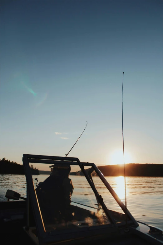 person on boat in lake with fishing pole at sunset