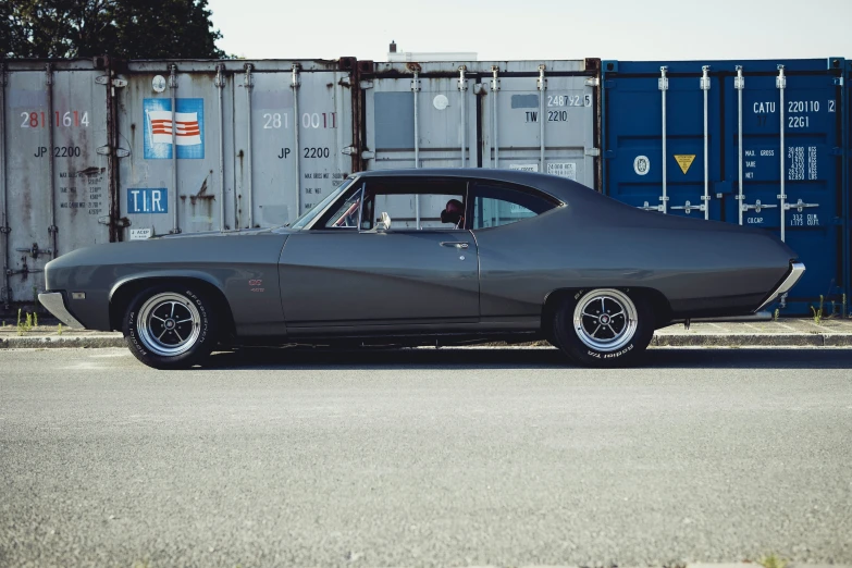 a large car is parked in front of some shipping containers