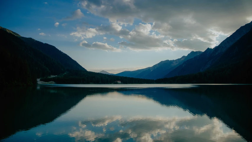 the mountains have clouds and the sky is reflecting in the water