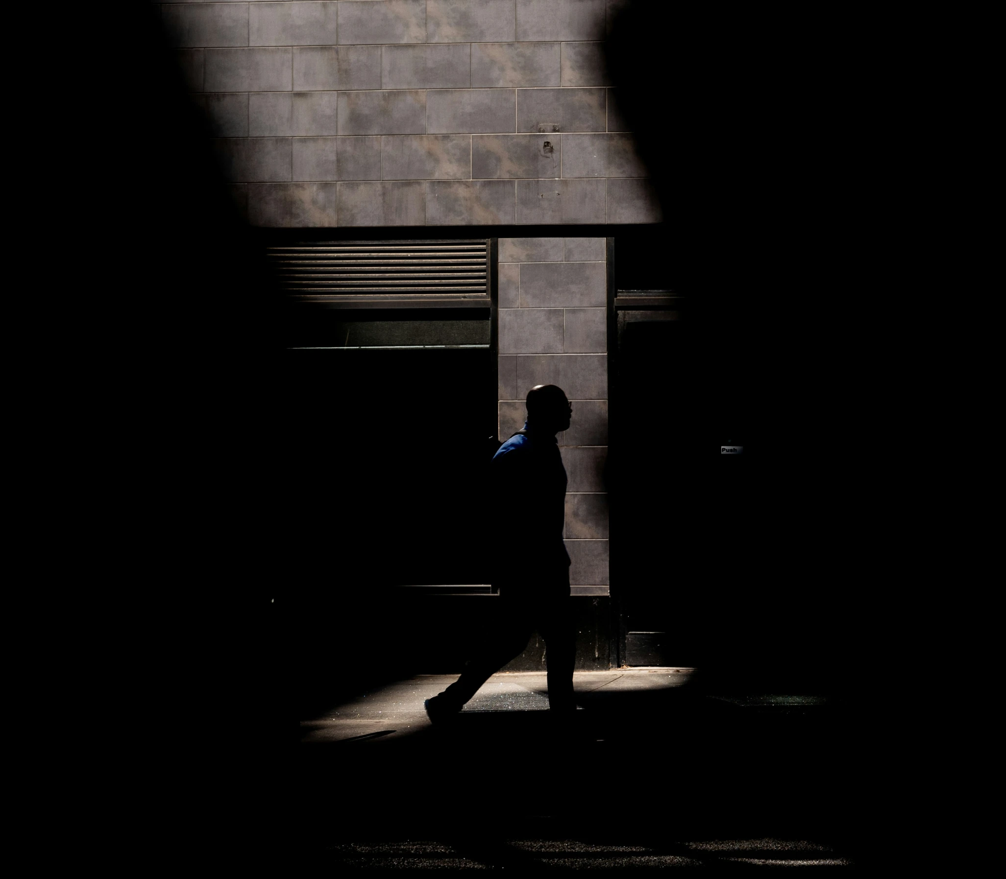 the shadow of a man walking on a sidewalk past a brick building