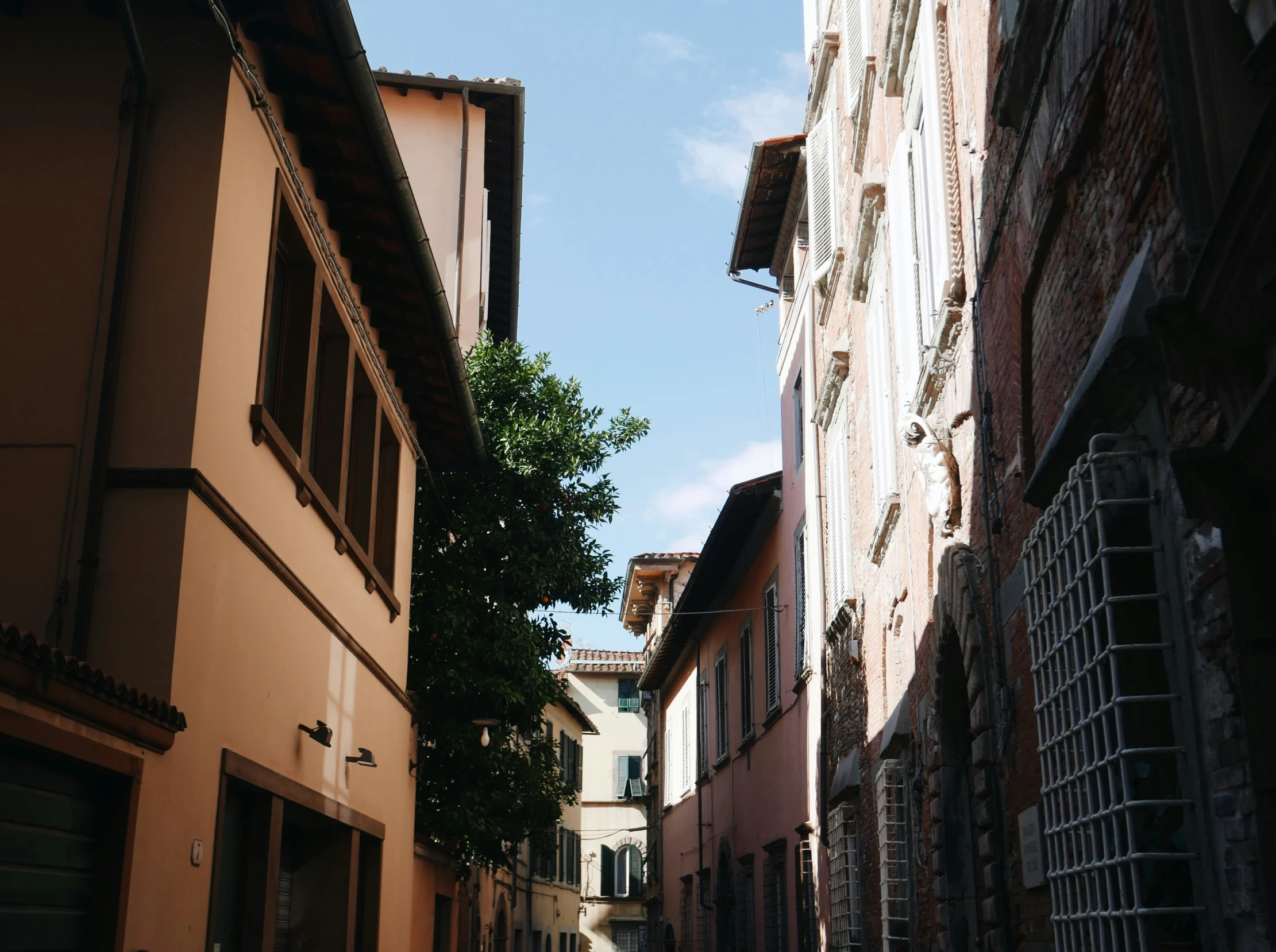 an alleyway has tall brown buildings and a blue sky