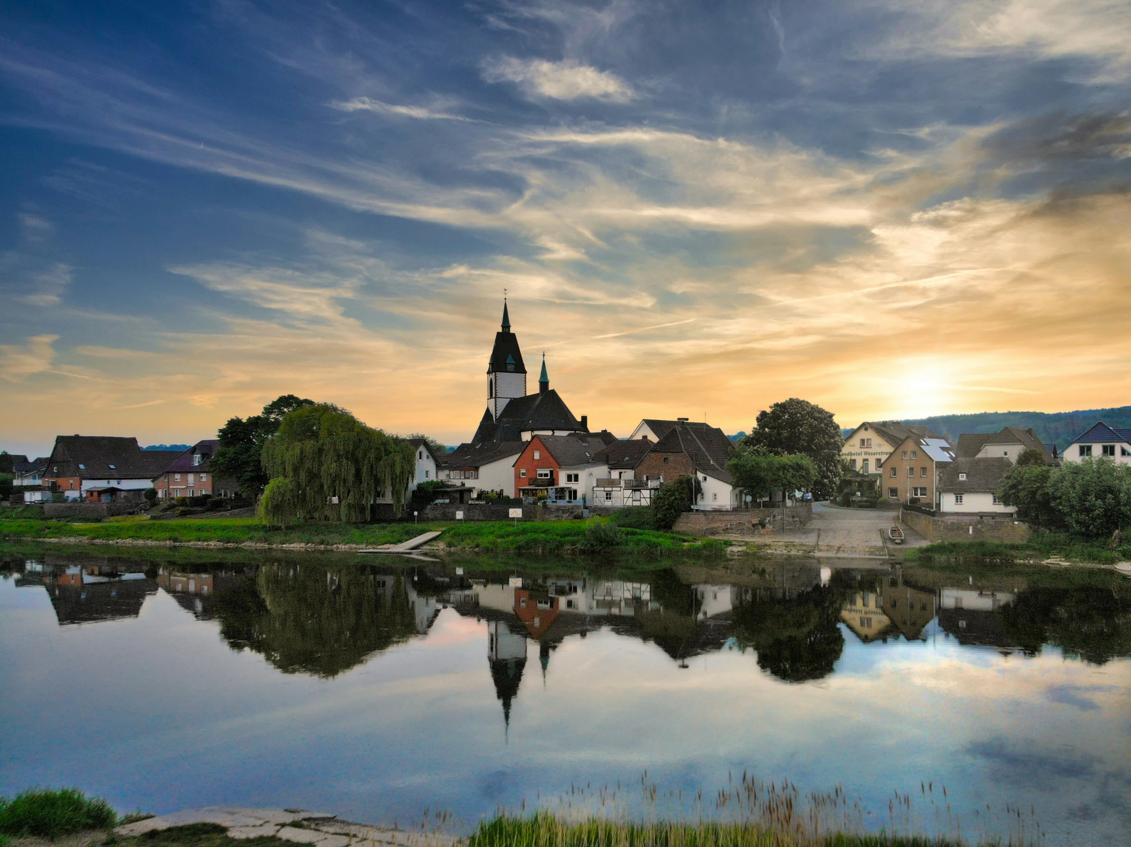 a very pretty town with a church tower next to a lake