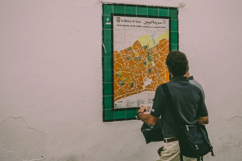 a young man standing against a wall with an outdoor map