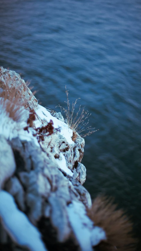 the corner of a small cliff and a body of water with snow on it