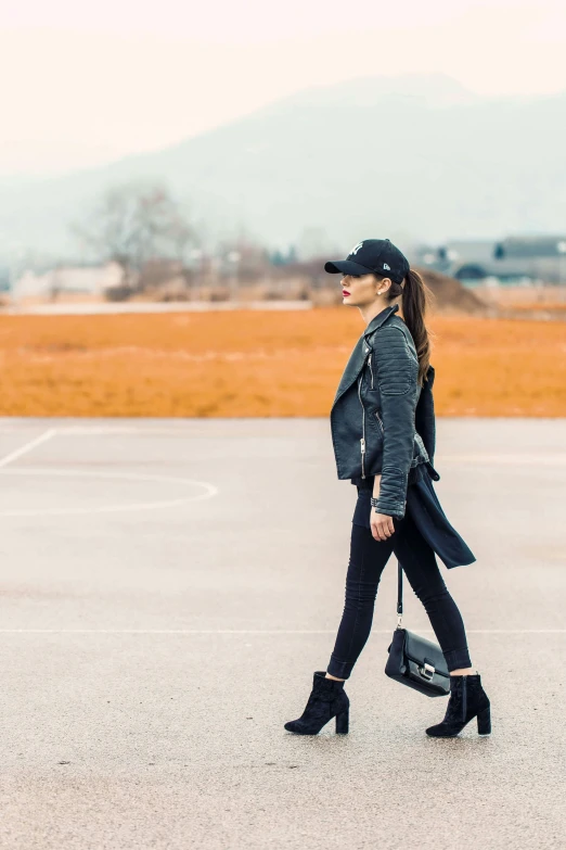 a woman walking across an empty tarmac while wearing a hat and boots