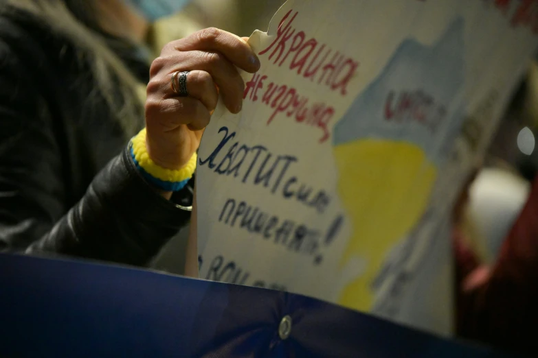 a man writing on a sign while holding a yellow and blue hat