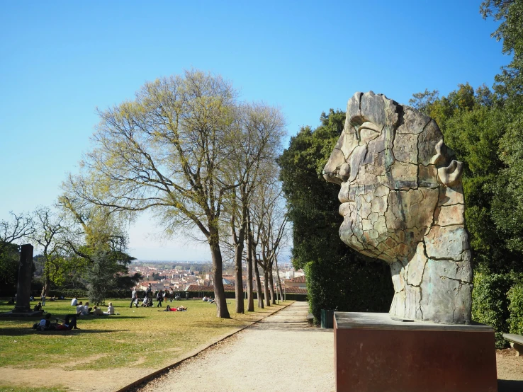 people sitting in the grass near trees and some stone sculptures