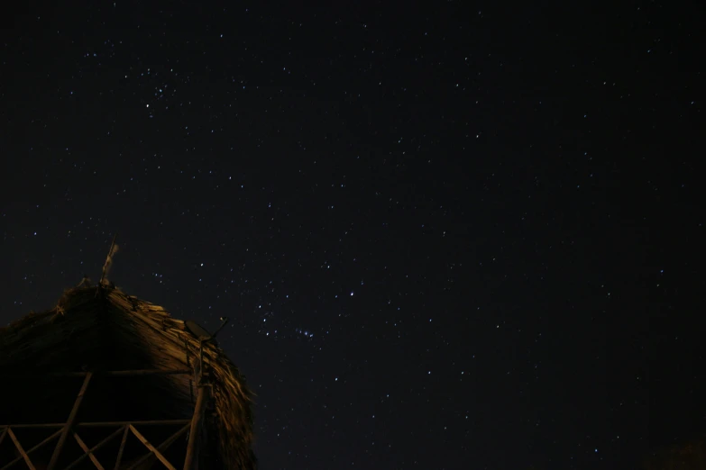 a night time po of the sky with stars above a structure
