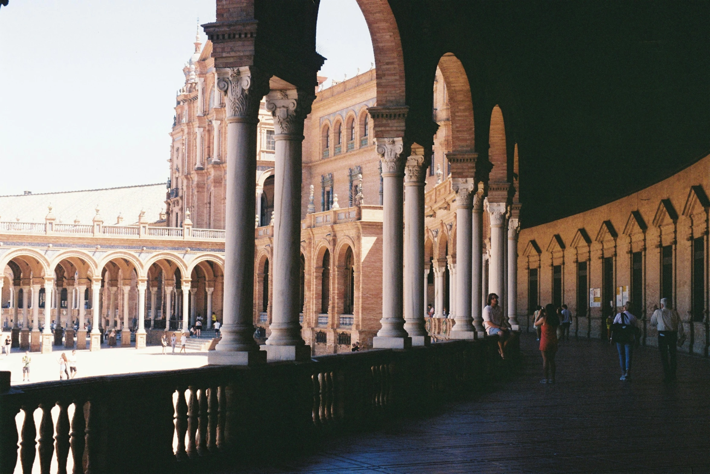 people walking along a large building under arches