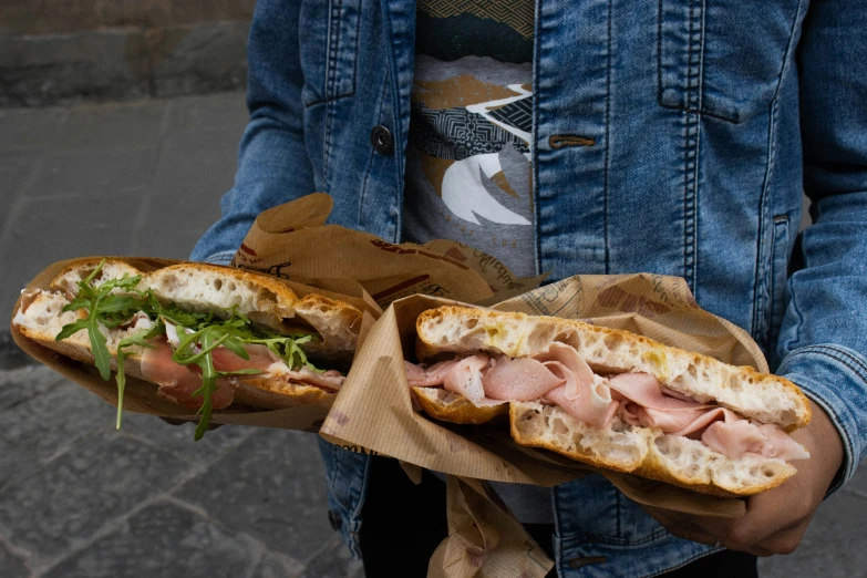 a person is holding a sandwich with ham and green lettuce