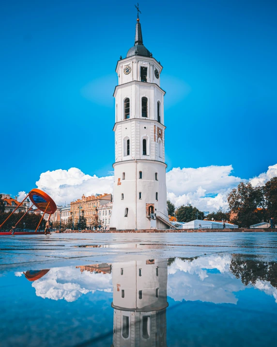 a tall white clock tower reflecting in the water