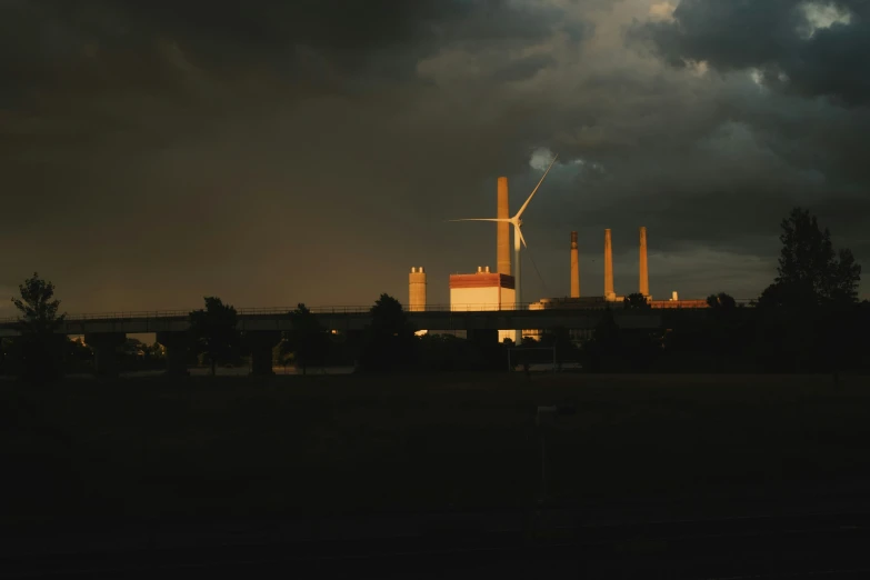 a dark sky over power plants with a bridge in the background