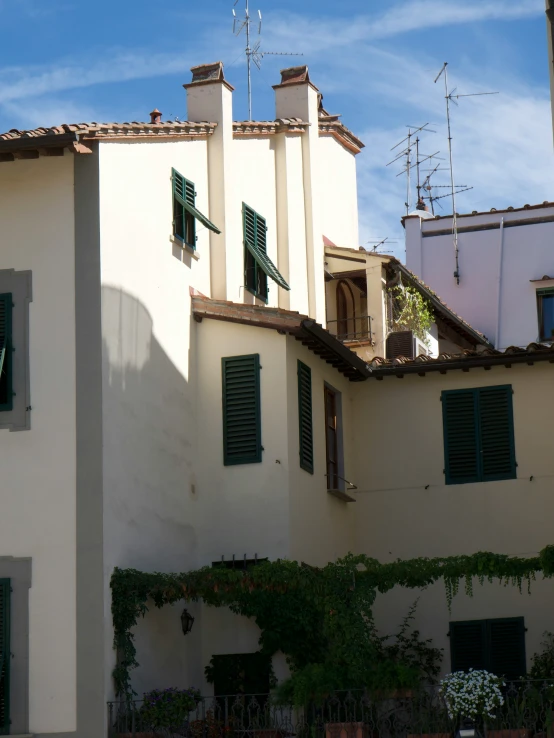 a building with shutters and windows has plants growing around