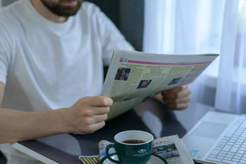 a man is looking at a newspaper while holding his coffee mug