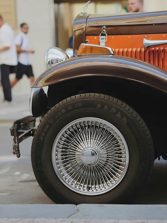 old model orange car on side of road with passengers walking past