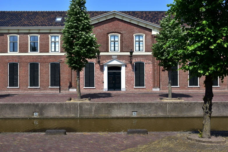 a red brick building with trees and a pond below it