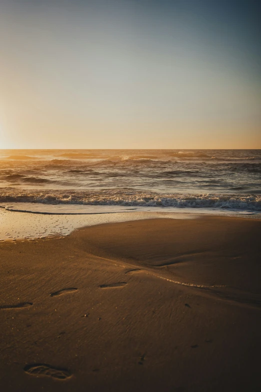 a sun setting over an ocean with footprints in the sand